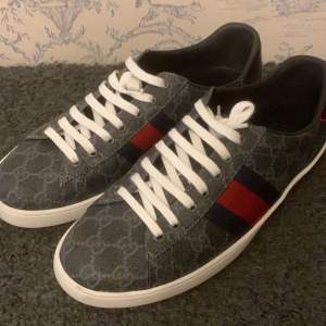 Säljer ett par Gucci Ace sneakers i storlek 43, nästan oanvända och i nyskick. Klassisk vit design med de ikoniska marinblå och röda ränderna. Perfekt för dig som vill ha lyxiga och tidlösa sneakers! Obs inget og