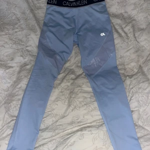 Calvin Klein träningsbyxor - Snygga träningstights från Calvin Klein i en ljusblå färg. Tighten har en bred resår i midjan med Calvin Klein-loggan. Det finns även en liten CK-logga på vänster lår. Tighten har en snygg design med mesh-paneler på sidorna.  Stl: S Nypris: 699