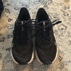 Svarta Nike Revolution sneakers - Säljer ett par svarta Nike Revolution sneakers. De har en snygg och enkel design med svart ovandel och vit sula. Skorna har snörning och är perfekta för träning eller vardagsbruk.