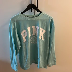 Turkos långärmad tröja från PINK - Säljer en superfin turkos långärmad tröja från PINK. Den har en stor vit text på framsidan och är perfekt för en avslappnad stil. Tröjan är i bra skick fast med en liten fläck under loggan på framsidan 