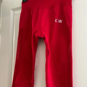 Röda leggings från ICANIWILL - Säljer ett par snygga röda leggings från ICANIWILL. De är högmidjade och har en tight passform, perfekt för träning. Materialet är syntetiskt och andas bra, vilket gör dem bekväma att ha på sig under intensiva pass. De har en stilren design med små perforeringar längs sidorna för extra ventilation. De är endast provade.
