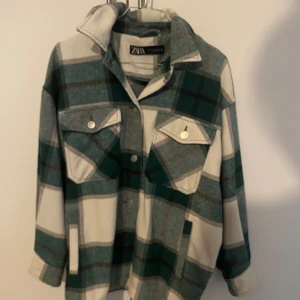 Rutig overshirt från Zara - Säljer en superfin rutig jacka från Zara i grönt och vitt. Den har långa ärmar och knappar framtill, samt två bröstfickor med knappar. Perfekt för höst och vår när du vill ha en stilren och bekväm look! den passar s och m även om det är xs i storlek då den är översized