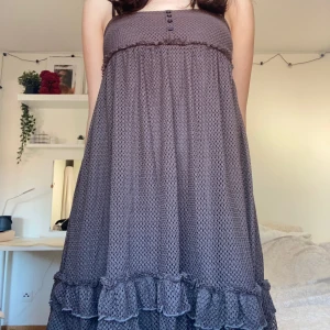 Brun klänning från Gina Tricot - Säljer en söt brun klänning från Gina Tricot i storlek XS. Klänningen har smala axelband och dekorativa knappar framtill. Den är i ett luftigt material med volangdetaljer längst ner, perfekt för sommarens varma dagar. Passar både till vardags och festliga tillfällen!