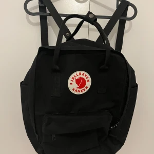 Svart ryggsäck från Fjällräven Kånken - Säljer en klassisk svart Fjällräven Kånken liknande ryggsäck i mycket bra skick. Den har det ikoniska runda märket på framsidan och en praktisk dragkedja. Perfekt för både skola och fritid!
