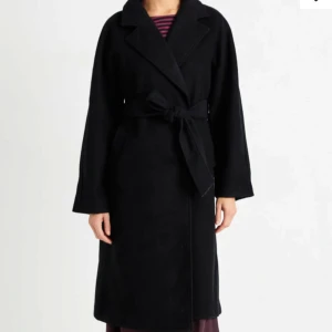 Svart kappa med knytband - Säljer en elegant svart kappa med knytband i midjan. Den har en klassisk design med långa ärmar och är perfekt för höst och vinter. Kappan är i mycket bra skick och passar både till vardags och fest. Perfekt för att hålla sig varm och stilren!