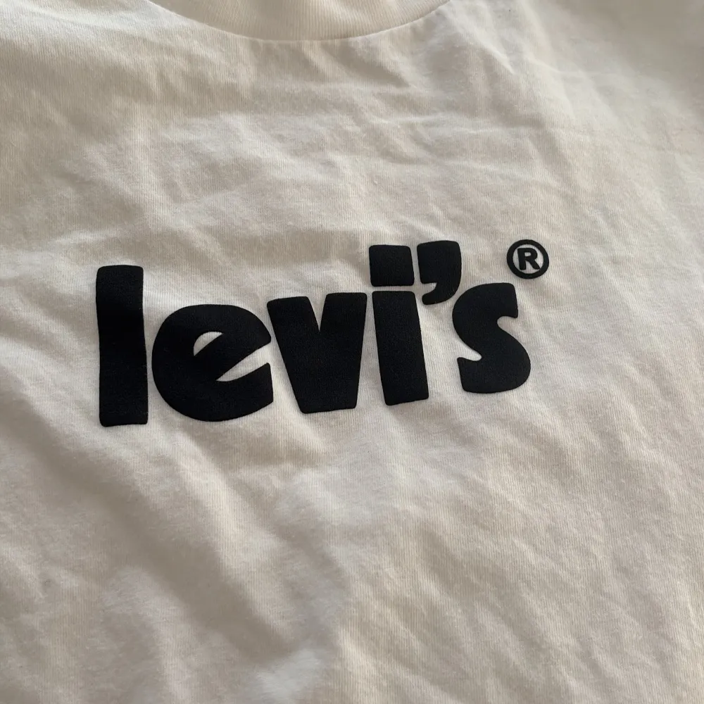 Säljer en klassisk vit t-shirt från Levi's i storlek XS. Den har en svart logga på bröstet och är gjord i mjuk bomull. Perfekt för en avslappnad stil eller som basplagg i garderoben. Kortärmad och i mycket bra skick!. T-shirts.