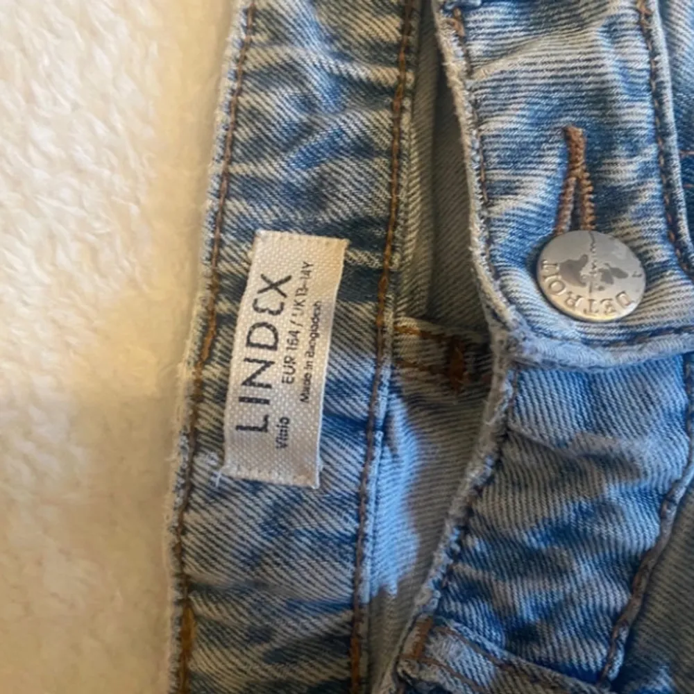 Säljer ett par ljusblå vida jeans från Lindex i okej skick. De har en klassisk femficksdesign med knapp och dragkedja framtill. Perfekta för vardagsbruk och kan matchas med det mesta i garderoben. Har ett litet hål vid fickan där bak. Storlek 164. Jeans & Byxor.