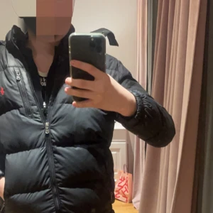 Svart pufferjacka från Polo Ralph Lauren - Säljer min polo jacka som är storlek xs och passar ungefär upp till 12-14 år. Den är i bra skick 8/10 enligt mig. Inga synliga defekter  Den är köpt på nk förra vintern. Den är även väldigt varm och bekväm med en fungerade luva osv. En perkfekt vinterjacka till vintern om du vill hålla dig varm samtidigt du har på dig något snyggt.  Om du har några frågor tveka inte på att skriva privat! Obs ( endast använd en vinter säsong) ‼️ passar ungefär till 163-169