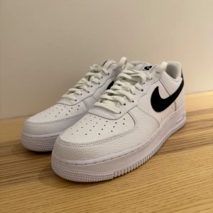 Nike Air Force 1 i vitt och svart - Säljer ett par klassiska Nike Air Force 1 i vitt med svart swoosh. Skorna är i nytt skick och har en stilren design med snörning. Perfekta för både vardag och fest! 🖤Som ni ser på bilderna är skorna aldrig använda då de var för stora, köpta direkt i fysisk butik. Kan gå ner i pris vid snabb och smidig affär! 