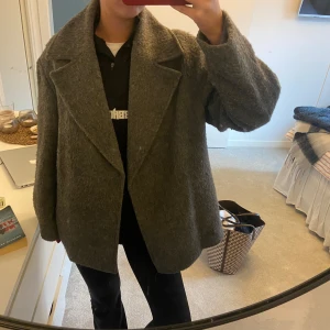 Grå ullkappa från H&M - Säljer en superfin grå ullkappa från H&M i storlek S. Den har en klassisk design med breda slag och en mysig, lite oversized passform. Perfekt för höst och vinter när du vill hålla dig varm och stilren. 🧥✨