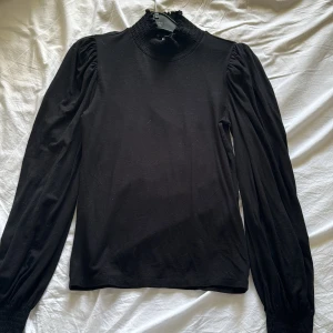 Svart långärmad topp från ONLY - Säljer en elegant svart långärmad topp från ONLY i storlek XS. Den har en ribbad hög krage och smockade ärmslut som ger en fin detalj. Perfekt för både vardag och fest! 🖤