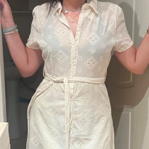 Vit klänning med broderade detaljer💛 - Säljer en superfin vit klänning med broderade mönster och knytband i midjan. Den har korta ärmar och en liten krage, perfekt för sommarens alla tillfällen. Klänningen har en slits framtill som ger en snygg touch. Passar både till vardag och fest!💛 Helt oanvänd samt bra material 💛Säljer pga att den sitter tajt på mig💛