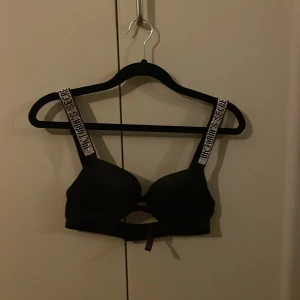 Svart bh från Victoria's Secret - Snygg svart bikiniöverdel från Victoria's Secret med breda axelband som har glittriga detaljer. ALDRIG använd då jag fick hem den i för liten storlek. Strlk 75B, har även i beige-rosa, röd och blå