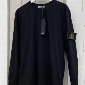 Säljer en stilren svart långärmad tröja från Stone Island. Den har en ikonisk logga på ärmen och är i nytt skick med etikett kvar. Perfekt för både vardag och fest. Passar bra till jeans eller chinos för en avslappnad men snygg look.