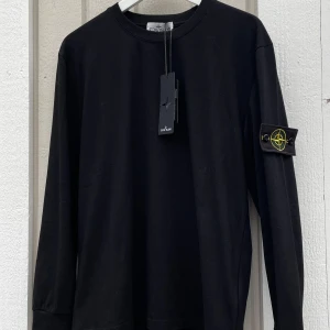 Stone Island Tröja - Säljer en stilren svart långärmad tröja från Stone Island. Den har en ikonisk logga på ärmen och är i nytt skick med etikett kvar. Perfekt för både vardag och fest. Passar bra till jeans eller chinos för en avslappnad men snygg look.