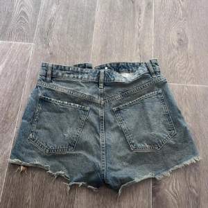 Säljer ett par coola jeansshorts i mycket bra skick. De är högmidjade med en rå kant och fransar längst ner för en avslappnad look. Perfekta för sommaren och festivaler! De har knappar framtill och klassiska fem fickor.