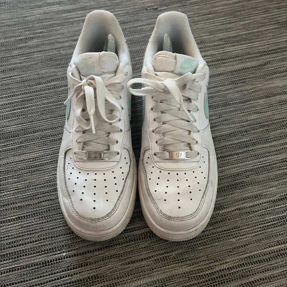 Säljer ett par Nike Air Force sneakers i vitt med mintgröna detaljer. Skorna har snörning och är i bra skick med lite slitage. Perfekta för vardagsbruk och ger en fräsch look till vilken outfit som helst.. Skor.