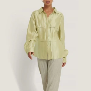 Blus - Snygg  blus med en elegant glans. Den har långa ärmar och knappar framtill, perfekt för både vardag och fest. Blusen har en klassisk krage och en lös passform som ger en avslappnad men stilren look.