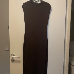 Brun klänning från Zara - Säljer en stilren brun klänning från Zara i storlek L. Klänningen är lång och har en enkel design utan ärmar, perfekt för både vardag och festligare tillfällen. Materialet känns mjukt och bekvämt mot huden. Ny med prislapp kvar, ursprungspris 299 SEK.