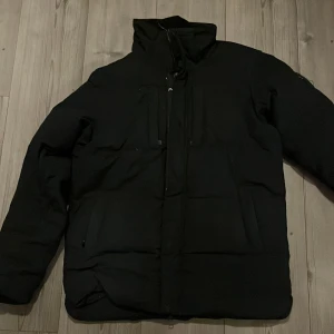 Svart vinterjacka - Säljer en svart vinterjacka i ett bra skick. Den har en hög krage och dragkedja framtill. Perfekt för kalla dagar och håller dig varm och bekväm. Passar både till vardags och utomhusaktiviteter. 