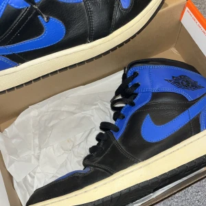 Nike Air Jordans i svart och blått - Säljer ett par Nike Air Jordans i svart och blått. Skorna har en klassisk design med snörning och är i mycket bra skick. Perfekta för både vardag och fest. De har en snygg kombination av svart och blått läder med den ikoniska Air Jordan-loggan på sidan.