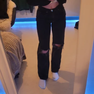 Svarta jeans med slitna knän - Säljer ett par svarta jeans i bra skick med coola slitningar på knäna. De är högmidjade och har en straight passform som ger en avslappnad look. Perfekta för både vardag och fest! 🖤