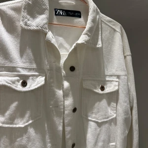 Vit manchesterjacka från Zara - Säljer en snygg vit manchesterjacka från Zara i storlek S. Jackan har en klassisk krage och knappar framtill. Den har två bröstfickor med knappar och är perfekt för höst och vår. Passar både till vardags och lite finare tillfällen. Superfräsch och i mycket bra skick!