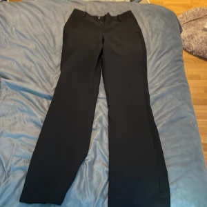 Svarta kostymbyxor från Bik Bok - Snygga svarta kostymbyxor från Bik Bok i storlek 34. De har en klassisk design med dragkedja och knapp framtill. Perfekta för både jobb och festliga tillfällen. Byxorna är i mycket bra skick och har en elegant passform.