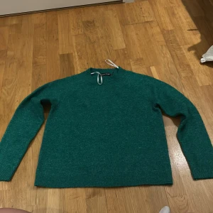 Grön stickad tröja från Pieces - Säljer en snygg grön stickad tröja från Pieces i storlek M. Perfekt för kyliga dagar med sin mysiga och varma känsla. Tröjan har en enkel design med ribbade kanter vid ärmslut och nederkant. Passar både till vardags och lite finare tillfällen.