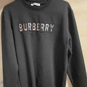 Vit t-shirt från Dsquared2 - Bild 1: Svart Burberry sweatshirt med klassisk Burberry-logga i mönstrad text på framsidan. Stilren och bekväm för en elegant vardagslook. Bild 2: Beige Hugo Boss t-shirt med en röd Hugo-logga på bröstet. Minimalistisk design som enkelt kan matchas med olika outfits. Bild 3: Vit Dsquared2 t-shirt med färgglada stänk och texten “ICON” tryckt stort på framsidan. Perfekt för en trendig och avslappnad stil.   De sammanlagda varorna  säljes för 800kr sammanlagt. Styck säljes för 300kr.