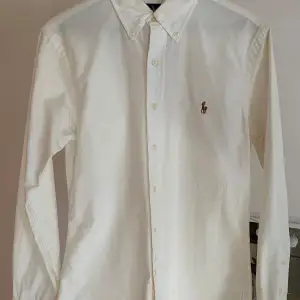 Säljer en klassisk vit skjorta från Ralph Lauren i slim fit. Skjortan är långärmad och har knappar framtill samt en broderad logga på bröstet. Perfekt för både vardag och fest! 🕺