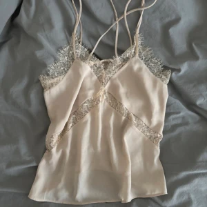 Beige linne från Bik Bok - Säljer ett supergulligt beige linne från Bik Bok. Det har tunna axelband och vacker spetsdetalj runt halsringningen och över bysten. Perfekt för sommardagar eller som ett lager under en kavaj. Knappt använd!
