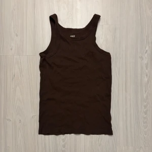 Brun ribbad tanktop från lager 157 - Säljer en brun tanktop från lager 157 i storlek S. Den är gjord av 100% bomull och har en enkel och stilren design. Perfekt för varma sommardagar eller som ett basplagg i garderoben. Toppen är i bra skick och redo för en ny ägare!