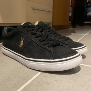Svarta sneakers från Ralph Lauren - Säljer ett par Ralph lauren skor i svart med vit sula. Brodererat på baksidan polo. Används mycket flitigt och aldrig blivit smutsig. Kan gå med på ett bra pris vid en snabb affär! Original box medföljer ej pga av att jag inte hittar den. Kvitto finns kvar!