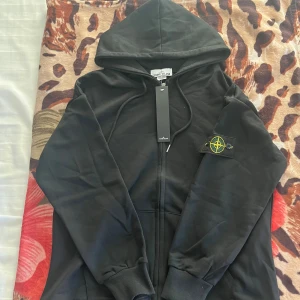 Stone Island Ziphoodie - Säljer en svart hoodie från Stone Island i nytt skick. Perfekt för höst och vår, med en skön passform och huva. Hör av er, DUNDER PRIS!!!🔥🔥