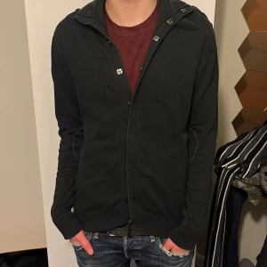 Svart kofta från Resteröds - Säljer en stilren svart kofta från Resteröds med knappar framtill. Perfekt för lager-på-lager och passar till många olika outfits. Koftan har långa ärmar och en klassisk krage.