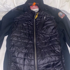 Svart quiltad jacka från Parajumpers - Snygg svart quiltad jacka från Parajumpers med dragkedja och broderad detalj på ärmen. Perfekt för kyligare dagar med sin stilrena design och praktiska fickor.