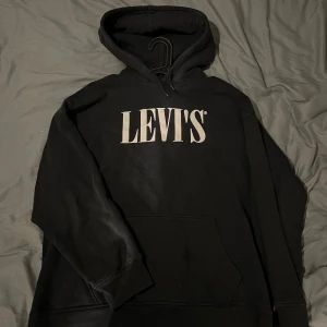 Mörk grå hoodie från Levi's - Säljer en mörk grå hoodie från Levi's med deras ikoniska logga tryckt på bröstet. Tröjan har en avslappnad passform och en klassisk känguruficka framtill.