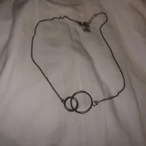 Halsband med dubbla ringar - Elegant halsband med två sammanlänkade ringar i silverfärg. Kedjan är tunn och justerbar, vilket gör det enkelt att anpassa längden. Perfekt för att lägga till en subtil touch av stil till din outfit.