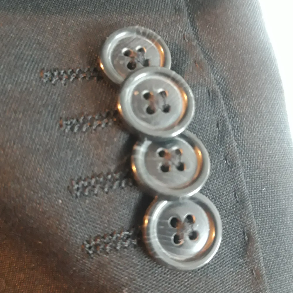 Snygg svart kavaj från Bläck med skräddarsydd passform. Kavajen har två knappar framtill och fyra dekorativa knappar vid ärmsluten. Perfekt för en stilren look.. Puvut & Bleiserit.