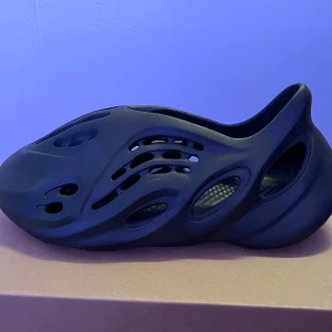 Svarta Adidas YZY Foam RNR - Säljer ett par svarta Adidas YZY Foam RNR med unik design och ventilerande hål. Perfekta för en modern och bekväm stil. Skorna är lätta och flexibla, vilket gör dem idealiska för vardagsbruk.