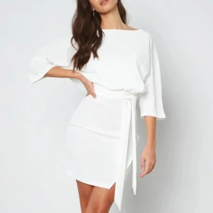 Vit klänning med knytband - Elegant vit klänning med trekvartsärmar och knytband i midjan. Den har en stilren design med en liten öppning i ryggen för en extra touch. Perfekt för studenten. Använd endast 1 gång