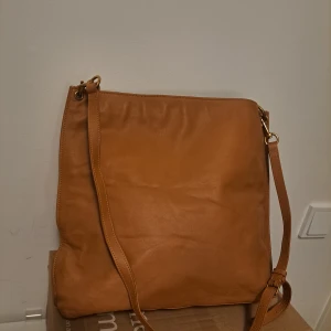 Brun axelväska i skinn - Snygg brun axelväska i skinn med justerbar axelrem och dragkedja upptill. Perfekt för vardagsbruk med stilren design.