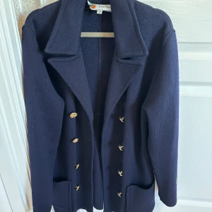 Mörkblå skepparkavaj från Busnel - Elegant mörkblå skepparkavaj från Busnel med guldknappar och klassisk krage. Perfekt för en stilren look. Kavajen har långa ärmar och två fickor framtill.