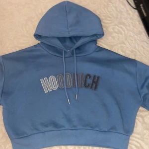 Hoodrich hoodie - Säljer en snygg blå hoodie från Hoodrich med tryck på bröstet. Den har en justerbar huva med dragsko och en croppad passform. Storlek M, ej använd 
