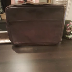 Brun datorväska i skinn Filippa K - Snygg brun datorväska i skinn med dragkedja. Perfekt för att bära din laptop med stil. Väskan har ett rymligt fack och en enkel design som passar till det mesta.