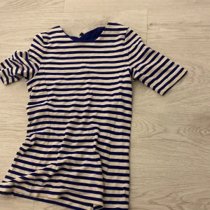 Randig klänning från COS - Säljer en stilren randig klänning från COS i blått och vitt. Klänningen har korta ärmar och en rund halsringning, perfekt för en avslappnad men chic look. Materialet är mjukt och bekvämt, vilket gör den idealisk för varma dagar.