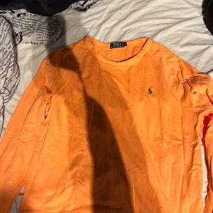 Orange långärmad tröja från Polo Ralph Lauren - Säljer en snygg orange långärmad tröja från Polo Ralph Lauren. Tröjan har en klassisk design med det ikoniska logotypen broderad på bröstet. Perfekt för en stilren och avslappnad look. Skick 10/10 säljer den på grund av att den aldrig använda pris kan diskuteras vid en snabb affär