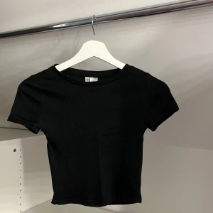 Svart ribbad topp från H&M Divided - Säljer en svart ribbad topp från H&M Divided. Toppen har korta ärmar och en rund halsringning, perfekt för en stilren look. Passar bra till både jeans och kjol.
