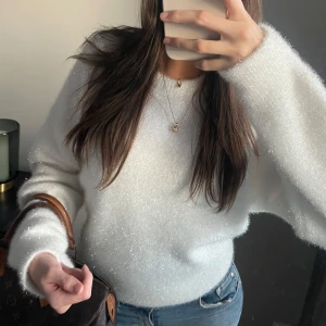 Vit fluffig glittrig tröja - Säljer en glittrig och fluffig vit oversize tröja med lång ärm. Perfekt för kyliga dagar när du vill känna dig både stilren och bekväm. Passar utmärkt till jeans eller kjol för en avslappnad look. 